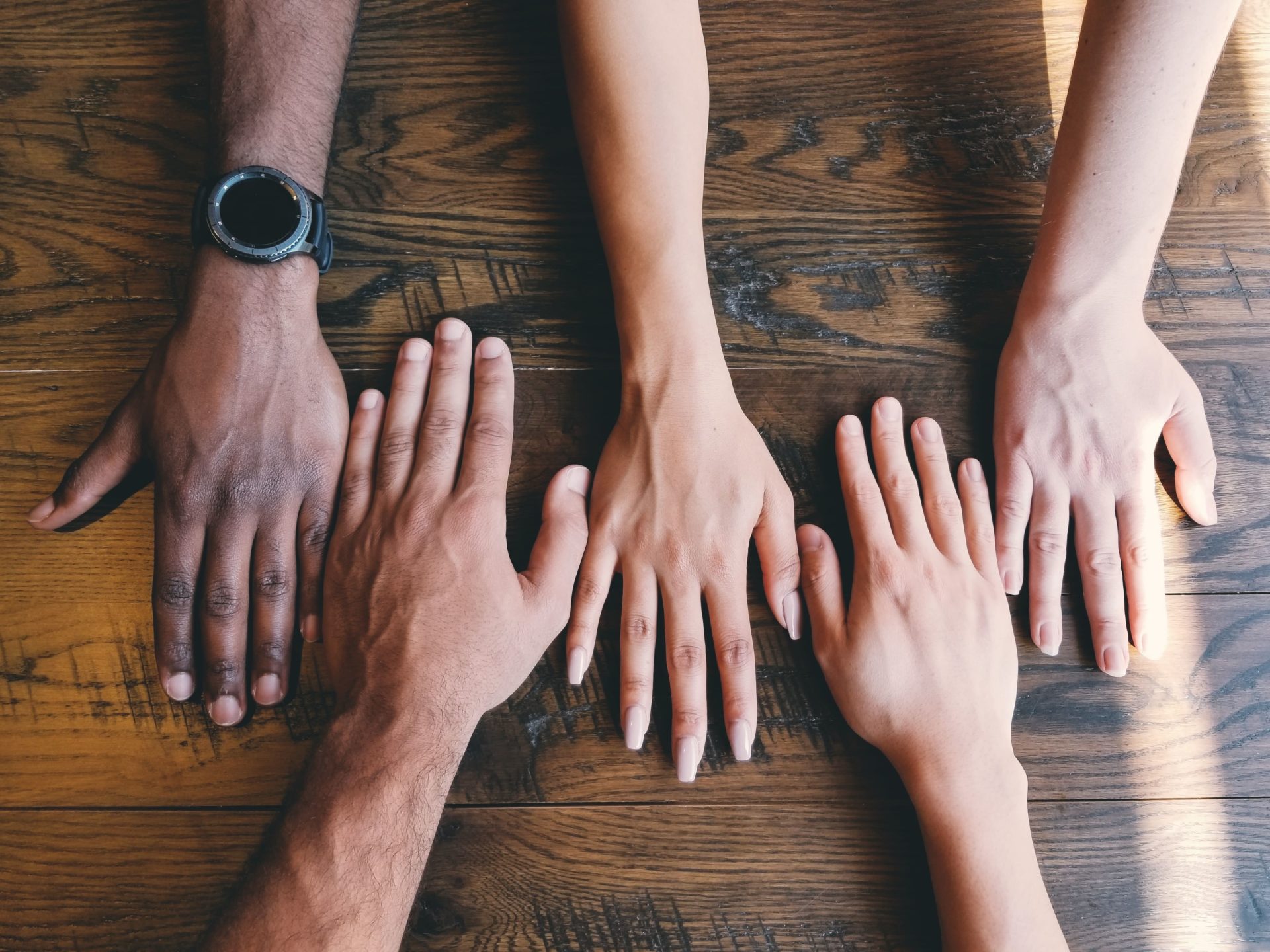 A line of different peoples hands laid on a desk to represent diversity